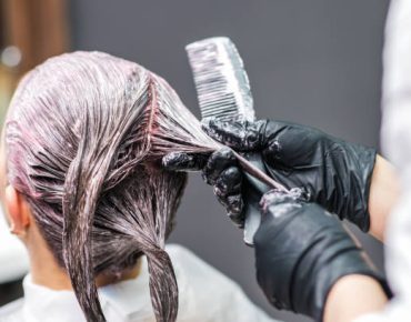 Close up back view of hairdresser is applying color to customer's hair in black gloves. Hair coloring in a beauty salon. Beauty and people concept.